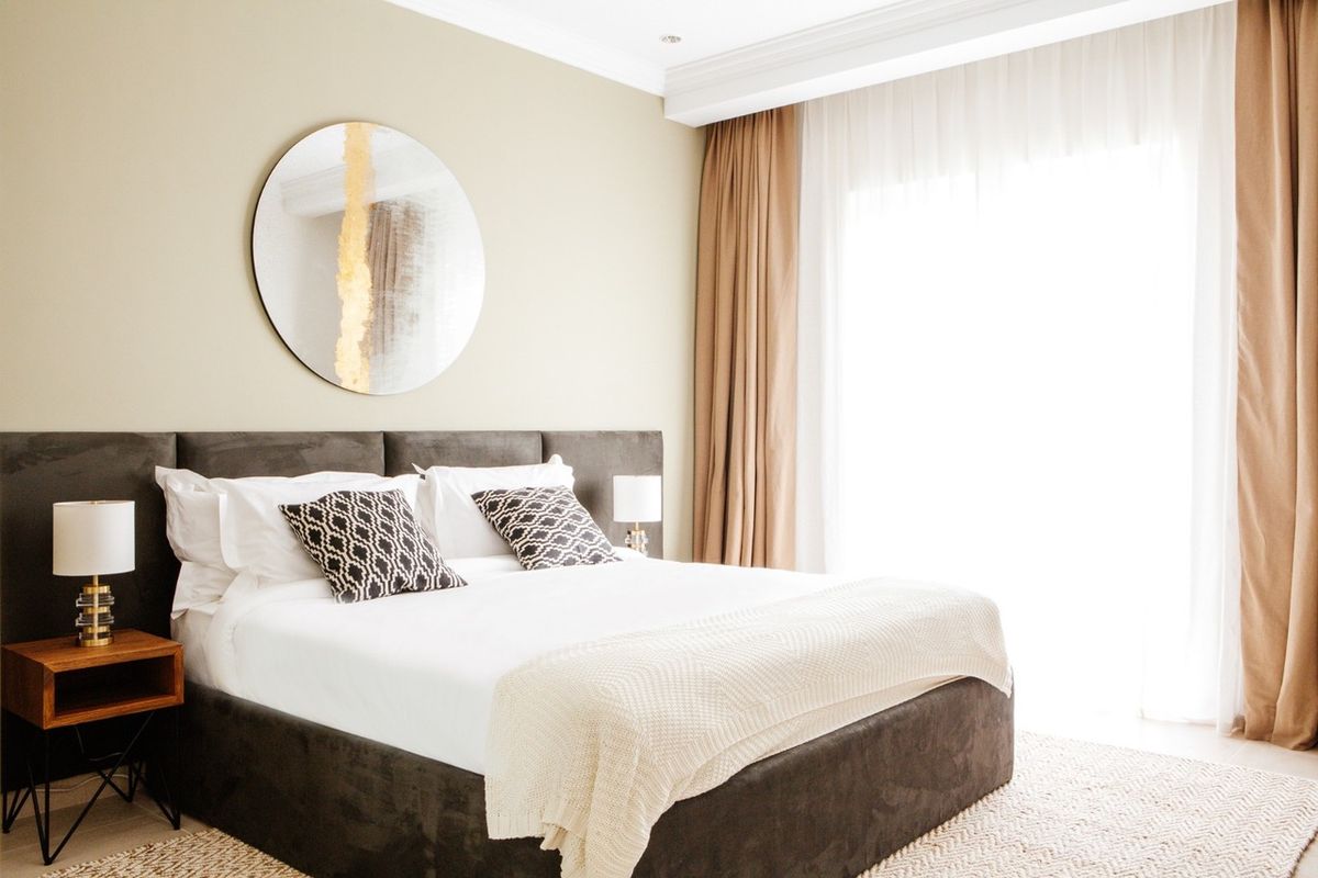 Bedroom with a grey velvet headboard and sand-coloured curtains